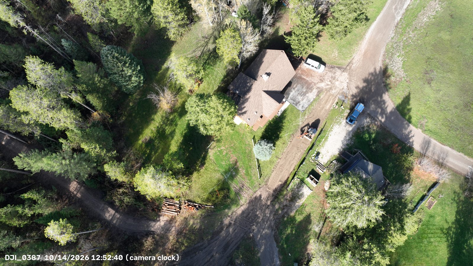 Drone photo showing the whole graded entrance from the street to where it meets the road up the hill, with a stack of logs beside the junction